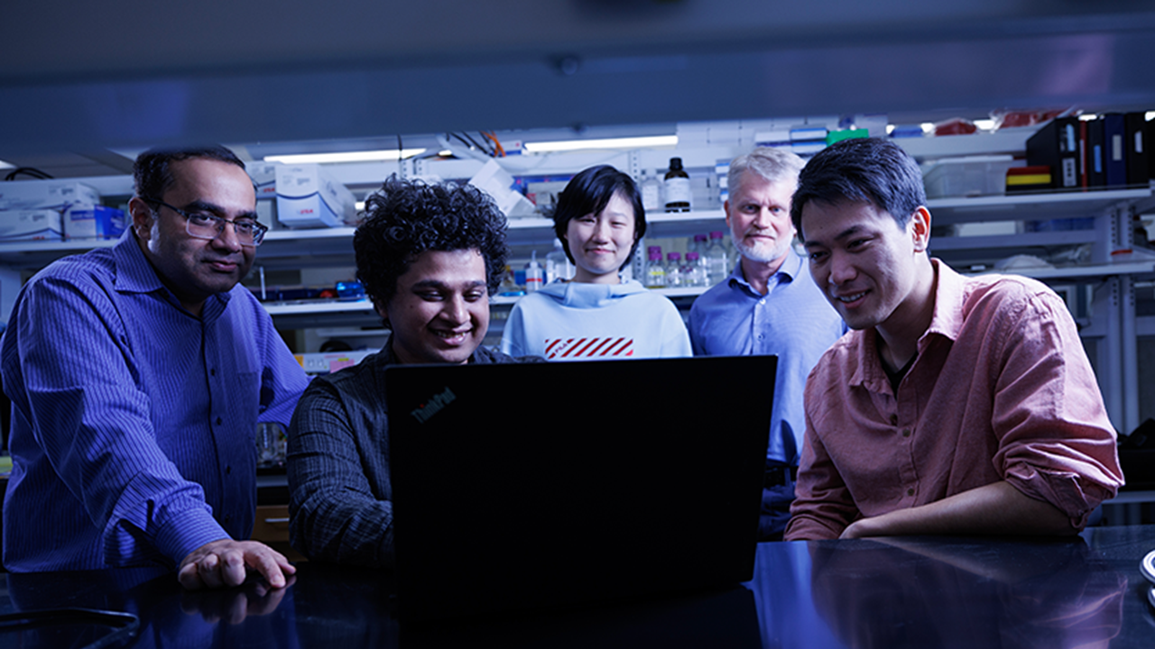 A group of lab researchers gather around a computer monitor, looking at data displayed on the screen.